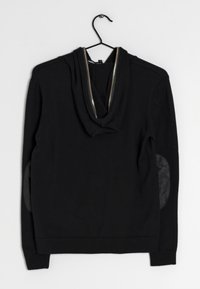 Sort langærmet sweatshirt med lynlås hætte og læderalbue-patches, hængende på sort bøjle mod hvid baggrund.