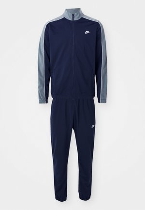 Fato de treino Nike azul-marinho feito de um tecido suave, apresentando uma jaqueta com fecho éclair e detalhes cinzentos, e calças com punhos elásticos e logotipo.