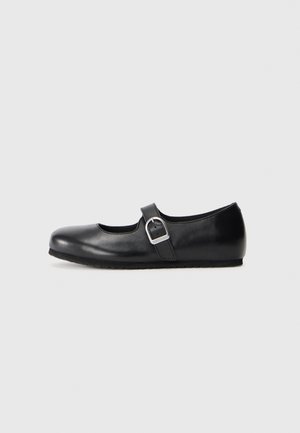 Chaussure plate Mary Jane en cuir noir avec un embout rond et une sangle à boucle en argent sur fond blanc.
