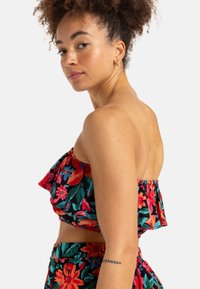 Blumen-Crop-Top mit gerüschten Kanten, verziert mit roten, rosa und blauen Blumen auf einem dunkelgrünen Hintergrund. Glatter Stoff und elastischer Bund.