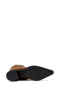 Stivale alla caviglia in suede marrone con forma affusolata, tomaia texturizzata e suola in gomma nera liscia con un battistrada lavorato per la presa.