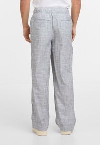 Svetle šedé kárované kalhoty s volným střihem, elastickým pasem a dvěma zadními kapsami. Materiál vypadá měkce s jemnou texturou.