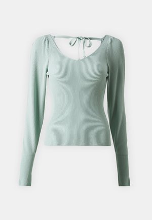 Prilagođena bluza s dugim rukavima u svijetlozelenoj rebrastoj tkanini. Ima V-izrez i detalj s vezanjem na leđima. Glatka tekstura s elastanom.