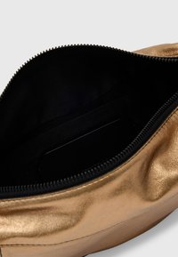 Metallisk guld pung med en glat tekstur, lynlåslukning og en sort stofindvendig. Har en sidelomme til organisering.