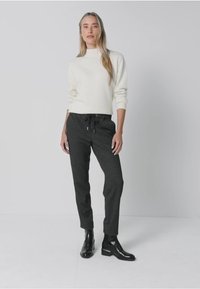 Bílý pletený svetr s vysokým výstřihem, zkombinovaný s tmavě šedými tepláky se stahovací šňůrkou a bočními kapsami, doplněný černými kotníkovými botami.