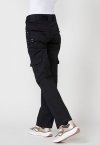 Pantalones cargo negros con bolsillos laterales, piernas rectas y un cinturón. Combinados con zapatillas deportivas blancas y doradas. Textura de tela suave.