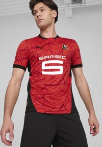 Camiseta de fútbol roja de manga corta con un patrón agrietado, acentos negros, cuello redondo y un gran número "6" en blanco en la parte delantera.
