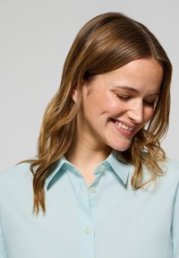 Jasnoniebieska koszula z kołnierzykiem, z zapięciem na guziki i haftowanym logo. Miękka tekstura z gładkim wykończeniem, posiada klasyczny krój i luźny fason.