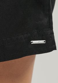 Shorts neri in cotone con orlo pulito, dotati di un'etichetta metallica argentea attaccata di lato che evidenzia i dettagli del marchio.