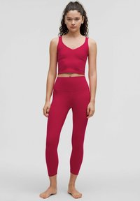 Top scurt, fără mâneci, ajustat, și colanți cu talie înaltă, de culoare roșu deschis, fabricați dintr-un material elastic, cu textură netedă, design minimalist, fără modele.
