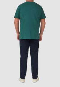 Donkergroen T-shirt met korte mouwen van zacht materiaal, gecombineerd met donkerblauwe broek. Het T-shirt heeft een ronde hals en een losse pasvorm.