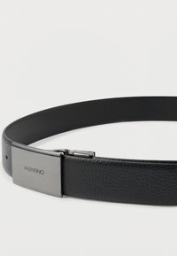 Črn usnjen pas z rectanglarno kovinsko zaponko, na kateri je vgravirano "VALENTINO" na svetli podlagi.