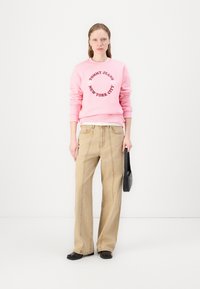 Rosa genser med trykket "TOMMY JEANS NEW YORK CITY" i mørkerødt, sammen med lysebeige vide bukser og svarte flate sko.