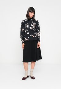 Blusa nera a fiori con maniche lunghe, abbinata a una gonna nera a lunghezza ginocchio e ballerine bordeaux. Il tessuto è morbido con un delicato motivo floreale.