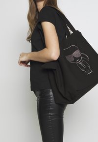 Black tote bag with a cartoon figure featuring glasses, embroidered in metallic thread. The bag has sturdy handles and a soft texture.