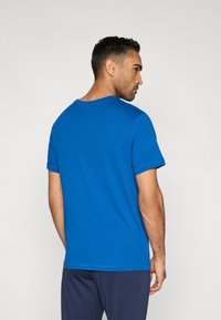 Μπλε βαμβακερό T-shirt με στρογγυλή λαιμόκοψη και κοντά μανίκια, με απαλή υφή. Φορώντας το με παντελόνι σκούρου χρώματος. Εμφανίζεται η πίσω όψη.