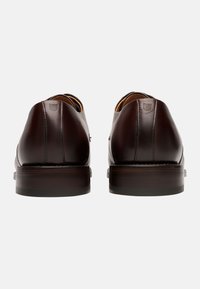 Chaussures en cuir marron avec une finition lisse, un bout arrondi et de minimalistes détails de couture ; la semelle en bois ajoute un contraste au design global.