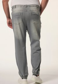 Pantalones jogger de mezclilla de color gris claro, con un ajuste relajado, cintura elástica y puños acanalados. Se pueden ver dos bolsillos traseros.