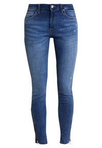Jeans ajustados de denim, en azul medio con un acabado desgastado. Presentan bolsillos frontales, un ligero desgaste y cremalleras en los tobillos.
