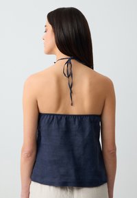 Top halter blu navy realizzato in tessuto leggero, con scollatura arricciata e legacci regolabili sul retro, dalla texture semplice.