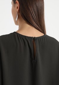 Black blouse featuring a round neckline with a small keyhole opening at the back, finished with a button detail and soft, flowing fabric.