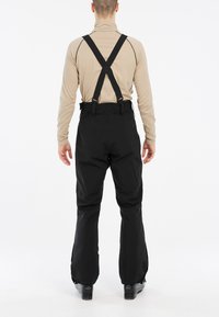 Pantalones impermeables negros con tirantes ajustables. Tienen un corte recto y relajado, y puños reforzados para mayor durabilidad.