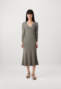 Robe ajustée à manches longues en tricot gris chiné avec un décolleté en V profond, ourlet évasé et boutons décoratifs sur les manches. Accompagnée de talons noirs.