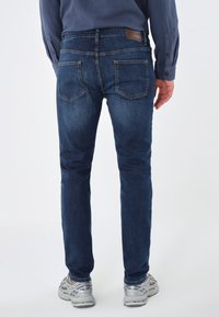 Tmavě modré džínové kalhoty s úzkým střihem, vybavené dvěma zadními kapsami, jemným šitím a hnědou koženou značkou na pásku.