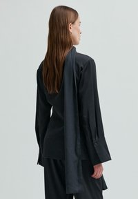 Černá dlouhá košile s pružným zadním panelem, zapínáním na knoflíky na zápěstí a hladkou strukturou, součást koordinovaného outfitu.