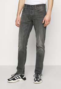 Gray denim jeans with a slim fit, featuring subtle fading, front pockets, and a standard waistband. Worn with black and white sneakers.