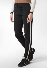 Zwarte joggingsbroek met witte zijstrepen, met een tailleband met trekkoord, slim fit en een gladde stofstructuur. Gemaakt met zwarte sneakers.