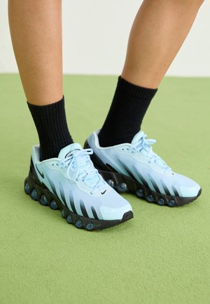 Des baskets Nike bleu clair avec des accents noirs, une tige en mesh et une semelle arrondie avec des pods transparents. Portées avec des chaussettes noires à côtes.
