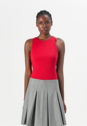 Haut sans manches rouge avec un col rond associé à une jupe plissée grise, mettant en valeur des textures lisses et des couleurs contrastées.