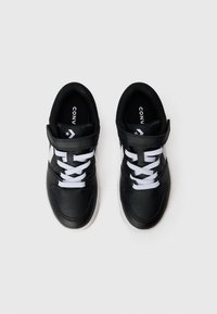 Svarta sneakers med en slät läderöverdel, vita snören och kardborreband. Har en ljus sula och subtila detaljer.