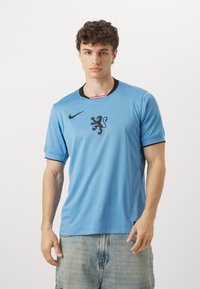 Maglietta sportiva azzurro chiaro con dettagli neri, caratterizzata da un emblema di leone e dal logo Nike sul petto. Design a maniche corte e collo a giro.