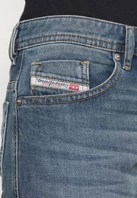 Blå denimjeans med en figurnära passform, med synlig sömnad, en bakficka med en Diesel Industry-etikett och en texturerad tyg.