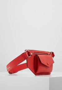 Borsa a cintura in pelle rossa con superficie testurizzata, tasca a zip sul davanti e una tasca più piccola con patta dotata di chiusura a scatto. Cintura regolabile.