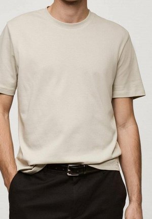 Beige T-Shirt mit kurzen Ärmeln und Rundhalsausschnitt, leicht in schwarze Hose mit schwarzem Ledergürtel gesteckt.