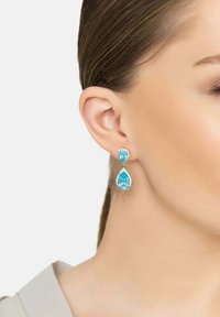 Pendientes en forma de lágrima que presentan dos piedras preciosas azules, una más grande y otra más pequeña, montadas en metal con tono plata y un detalle brillante.