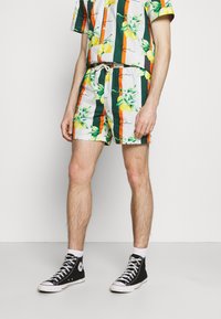 Set van wit T-shirt met korte mouwen en korte broek met groene strepen, gele citroenprints en oranje accenten. Gecombineerd met zwarte hoge sneakers.