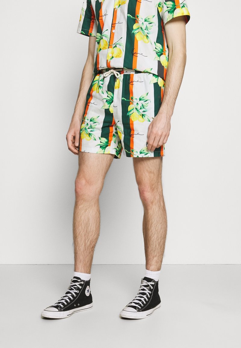 Set van wit T-shirt met korte mouwen en korte broek met groene strepen, gele citroenprints en oranje accenten. Gecombineerd met zwarte hoge sneakers.