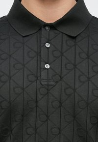 Polo nera con motivo testurizzato di forme geometriche in rilievo, tre bottoni al colletto e design del colletto strutturato.