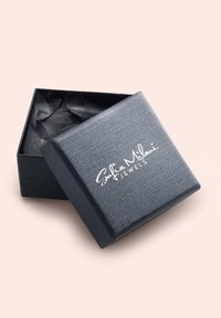 Svart strukturerad smyckeslåda med en silverlogo, delvis öppen för att avslöja mörkt silkespapper inuti. Fyrkantig form, minimalistisk design.