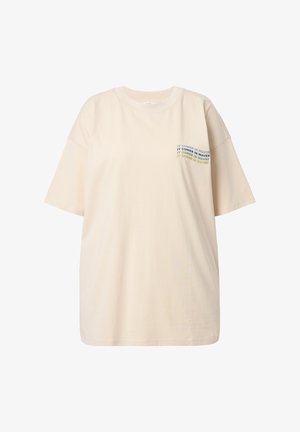 T-shirt surdimensionné de couleur crème en coton doux, avec des manches courtes et un graphique sur la poitrine comportant un texte multicolore qui dit "ÇA ARRIVE EN VAGUES."