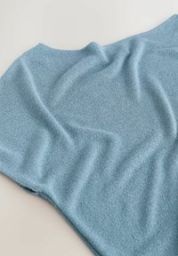 Tissu bleu clair à texture douce étalé à plat avec de légers plis sur un fond neutre clair.