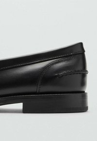 Mocassino in pelle nera con finitura liscia, tacco basso impilato e dettagli cuciti lungo il bordo superiore e i lati.