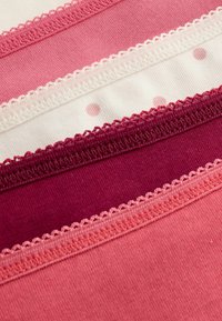 Vier stoffen stroken in verschillende tinten roze, met kanten rand, effen kleuren en één met witte stippen op een lichte achtergrond.