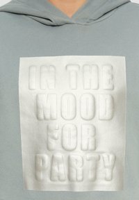 Lichtgrijze hoodie met een verhoogde witte tekstafdruk met de tekst "IN THE MOOD FOR PARTY" op de borst. Zacht materiaal met een ontspannen pasvorm.