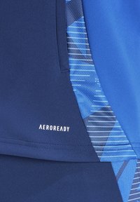 Tessuto atletico blu con motivi geometrici in diverse tonalità di blu. Presenta il marchio "AEROREADY" in bianco. Texture liscia.