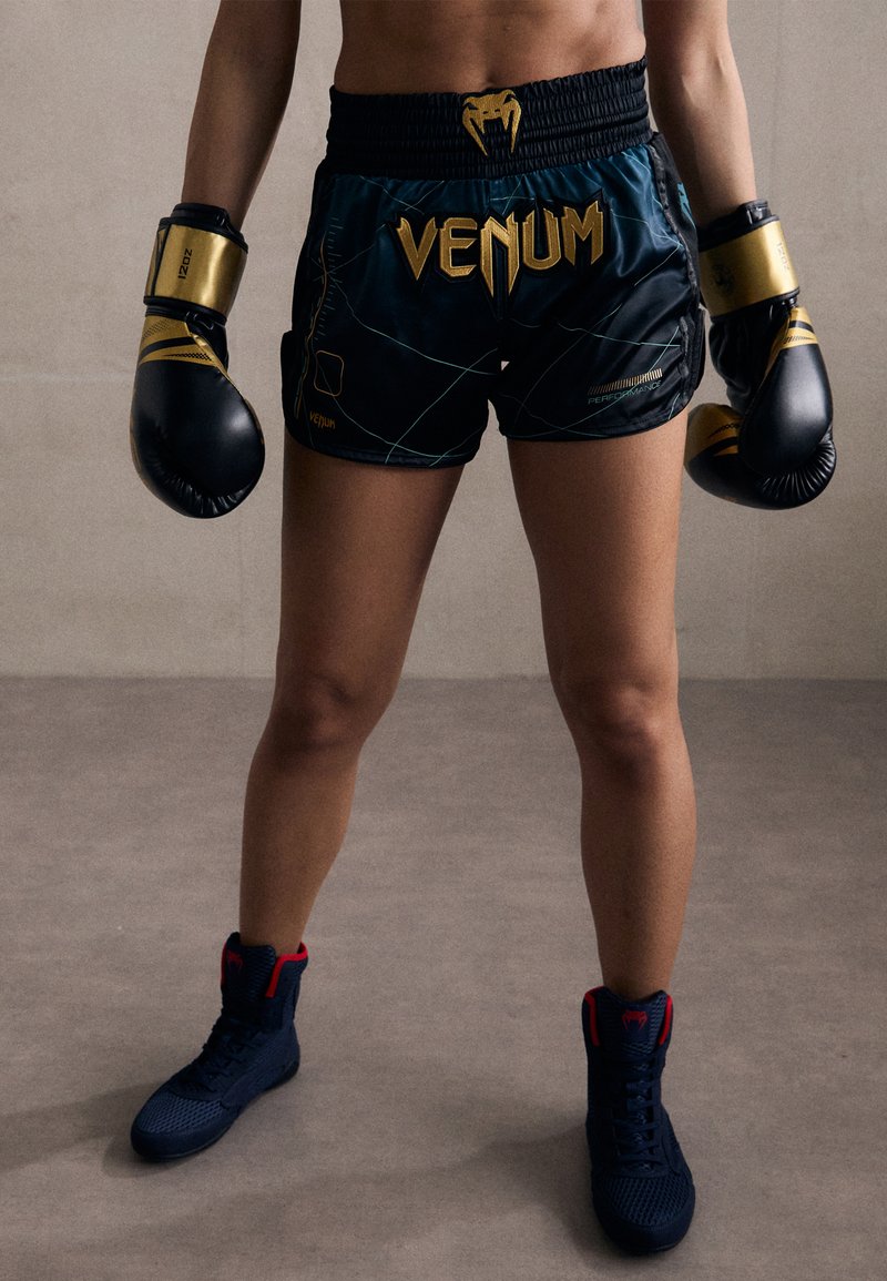 Μαύρες πυγμαχικές σορτς με χρυσό λογότυπο "Venum", που συνδυάζονται με μαύρα και χρυσά γάντια πυγμαχίας. Ναυτικές υποδήσεις με κόκκινες λεπτομέρειες και σχέδιο ψηλού κορμού.